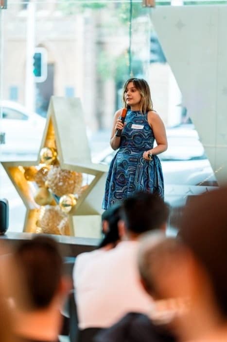 Nina, founder of MadeApt, speaking at an event in a MadeApt piece featuring Yankirri Jukurrpa by Ricardo Jampijinpa Gallagher