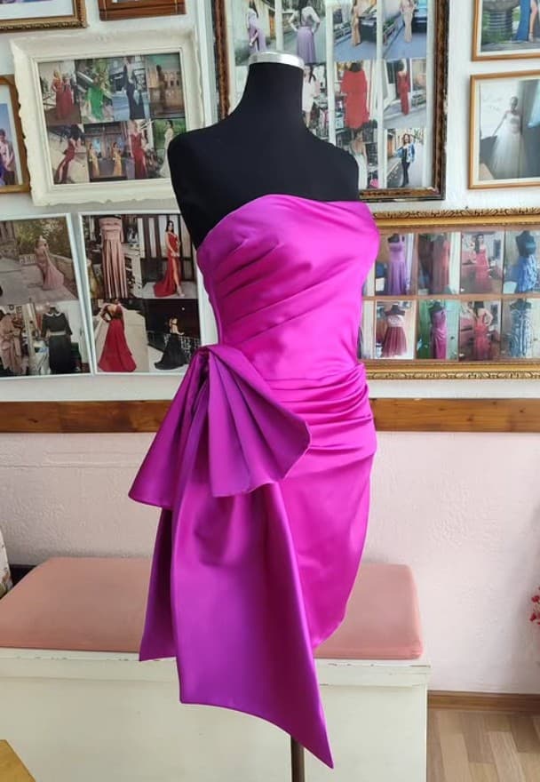 A fuchsia satin dress with a sculptural bow taking shape on a mannequin in the tailor's studio