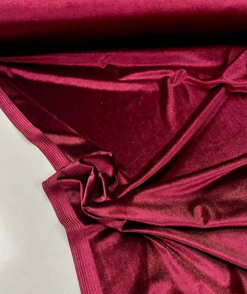 Burgundy stretch velvet unrolled on a cutting table, showing its pile, weight and sheen