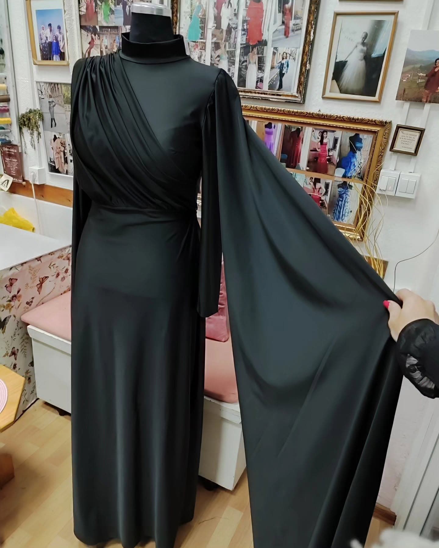 A custom black high-neck gown with a draped cape sleeve