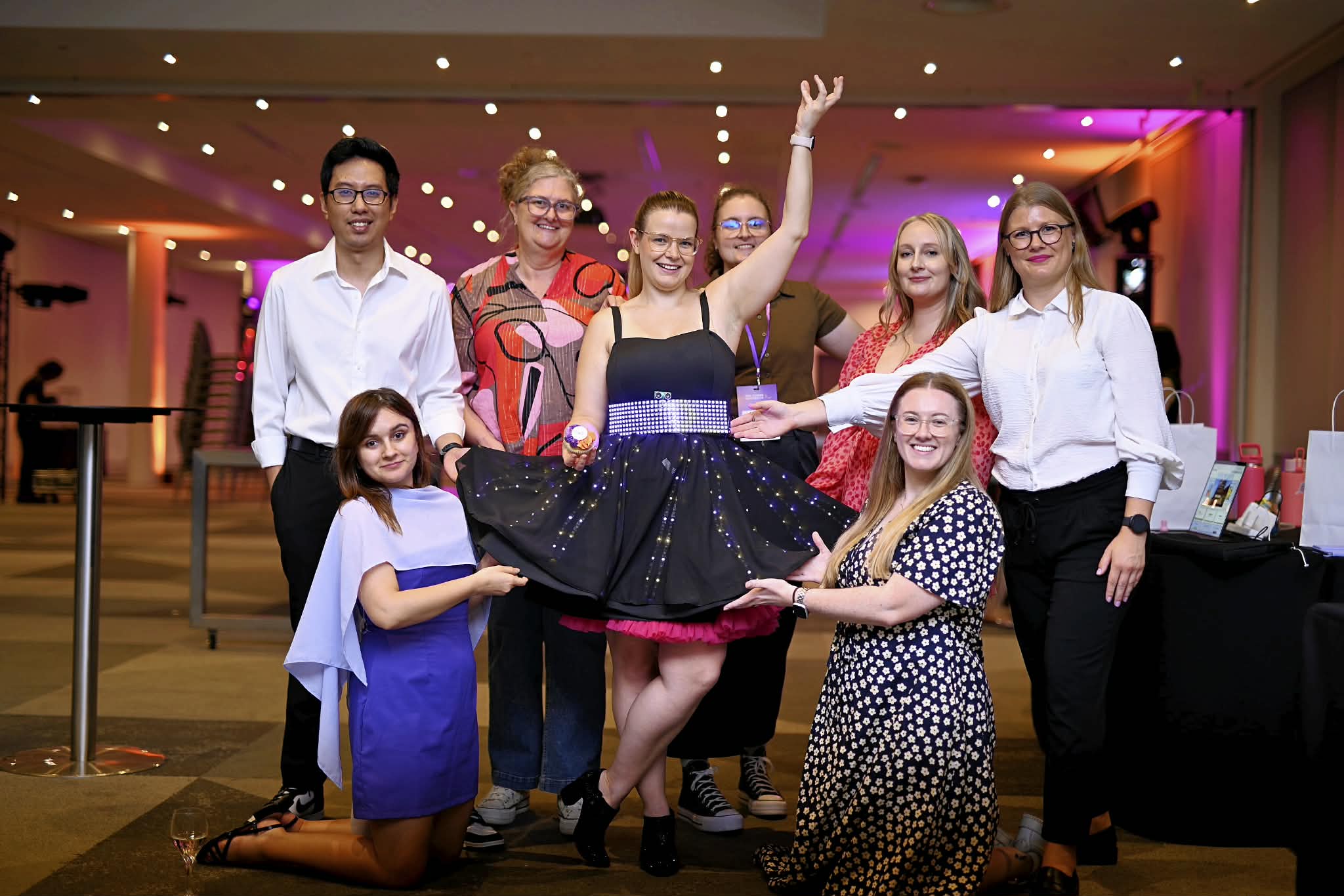 Kate at the centre of a group of She Codes people, arm raised, while two of them hold out the lit skirt