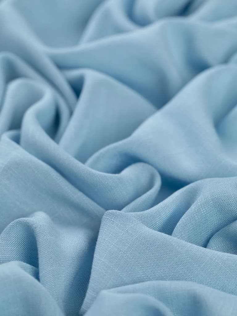 Pale blue linen cloth in crisp folds, the visible weave that gives linen its slightly sculptural hand