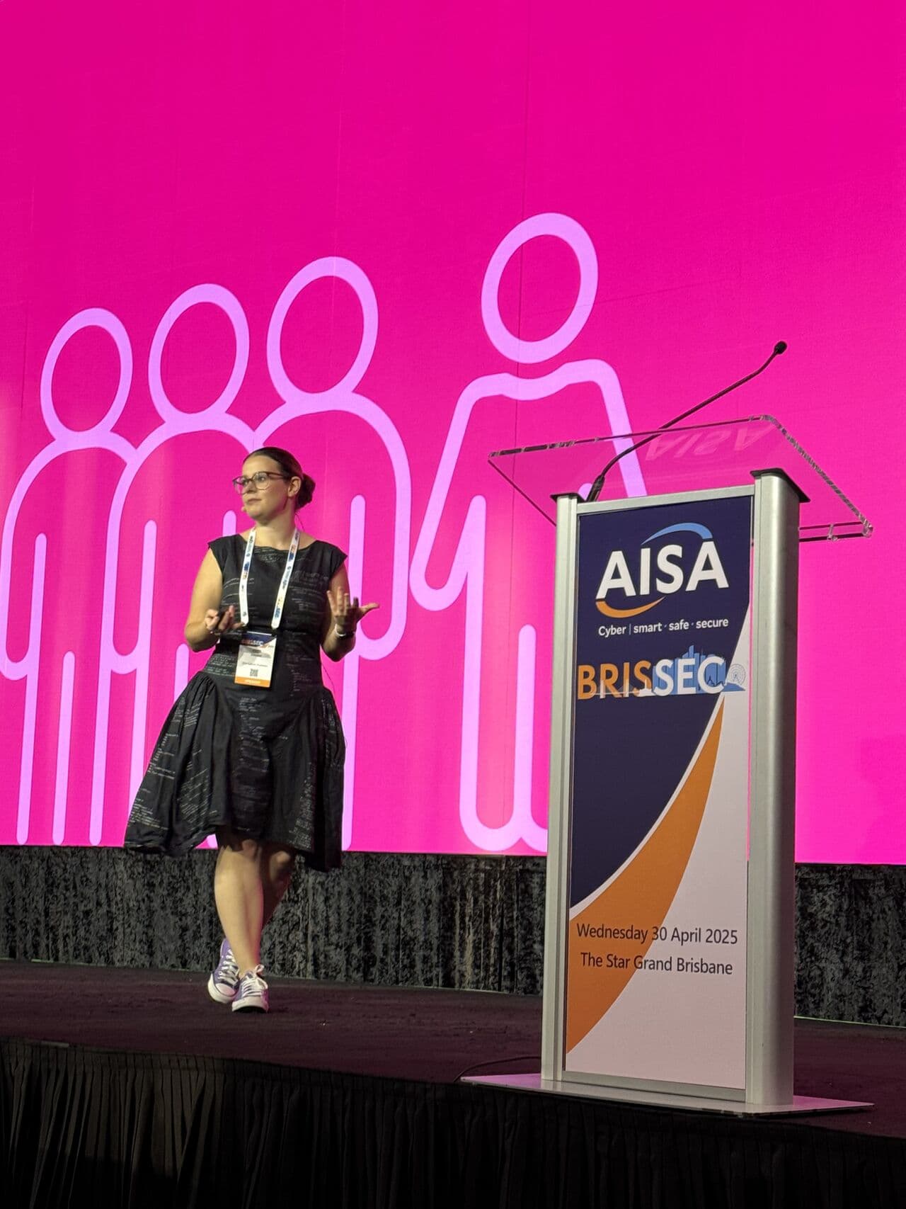 A performer in a dark textured dress on stage against a hot pink backdrop — the colour separation makes her read clearly