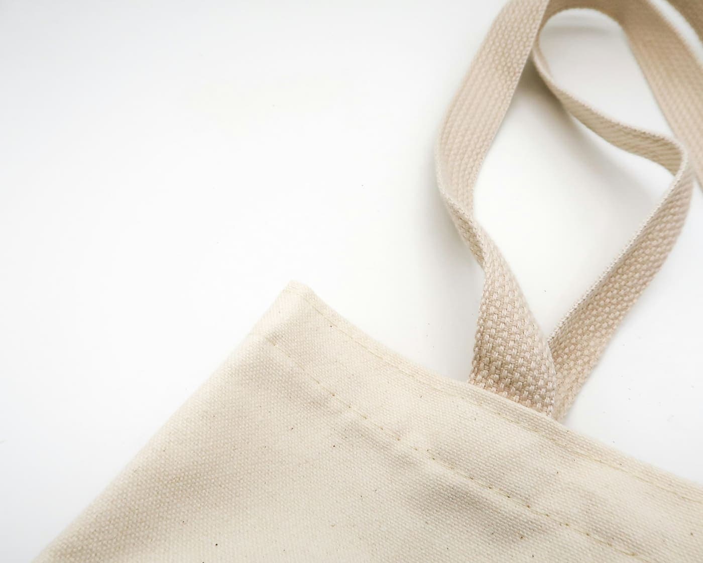 Close-up of a natural cotton canvas tote bag, showing the woven handle and the stitched seam where it joins the body