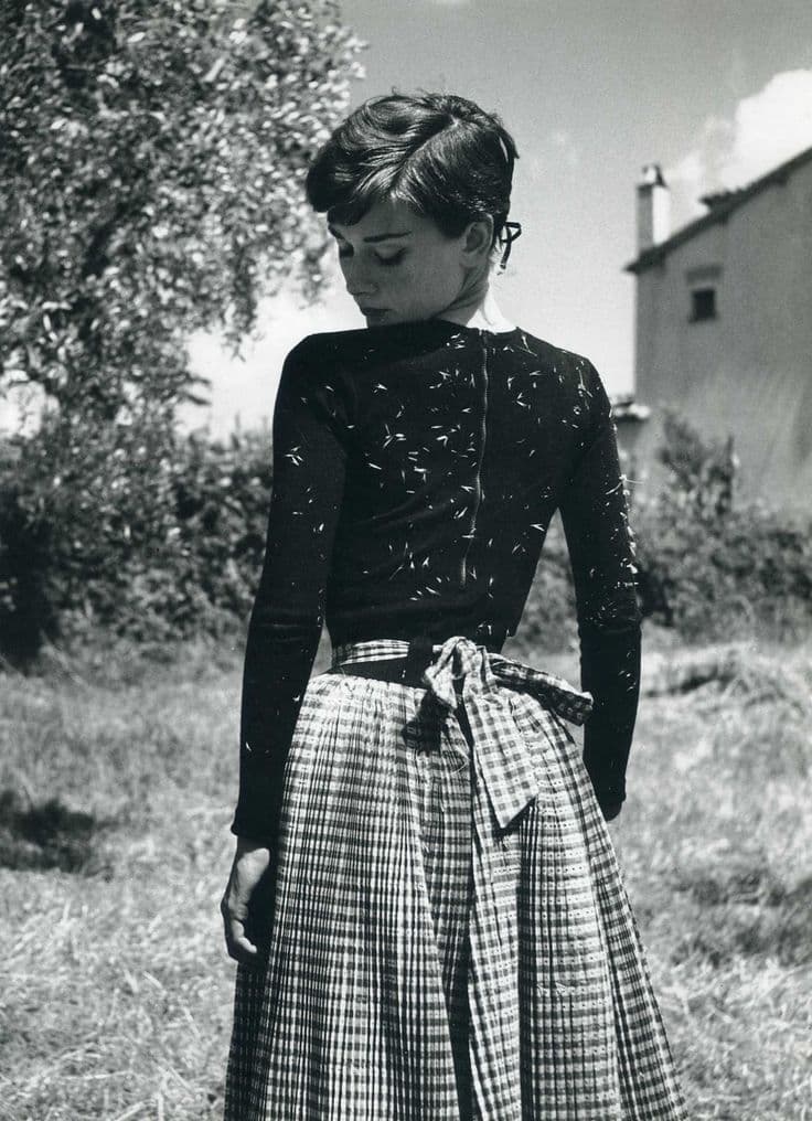 A black-and-white portrait in a fitted dark top and full checked skirt — a signature look
