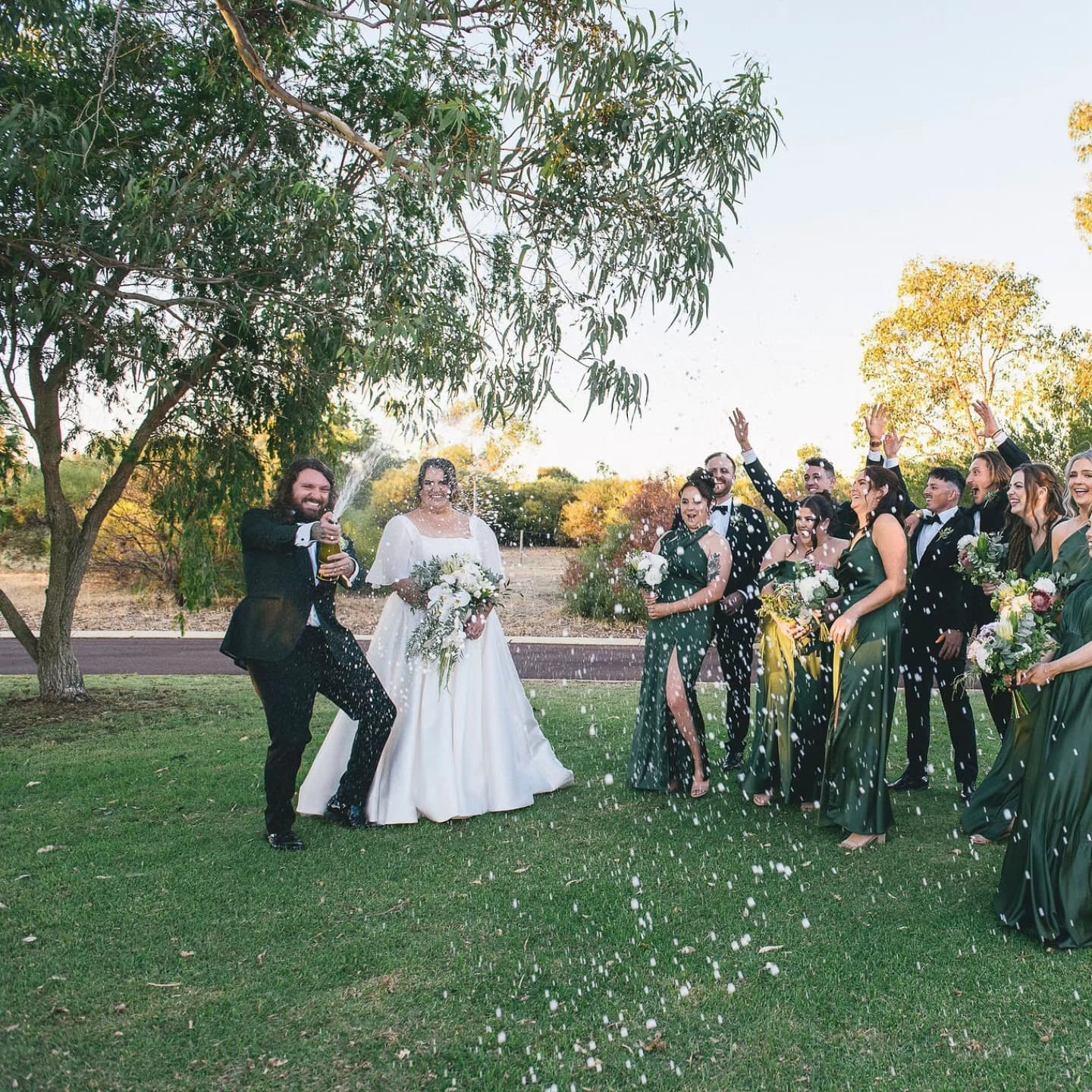 A bride with her bridesmaids in matching forest green custom bridesmaid dresses by the water