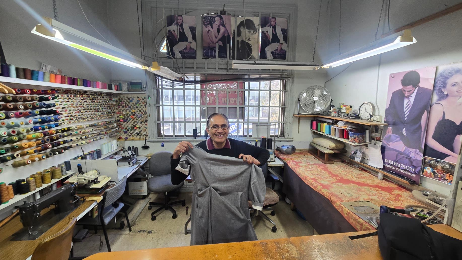 A tailor in his atelier holding a toile — the test garment fitted before the real fabric is cut