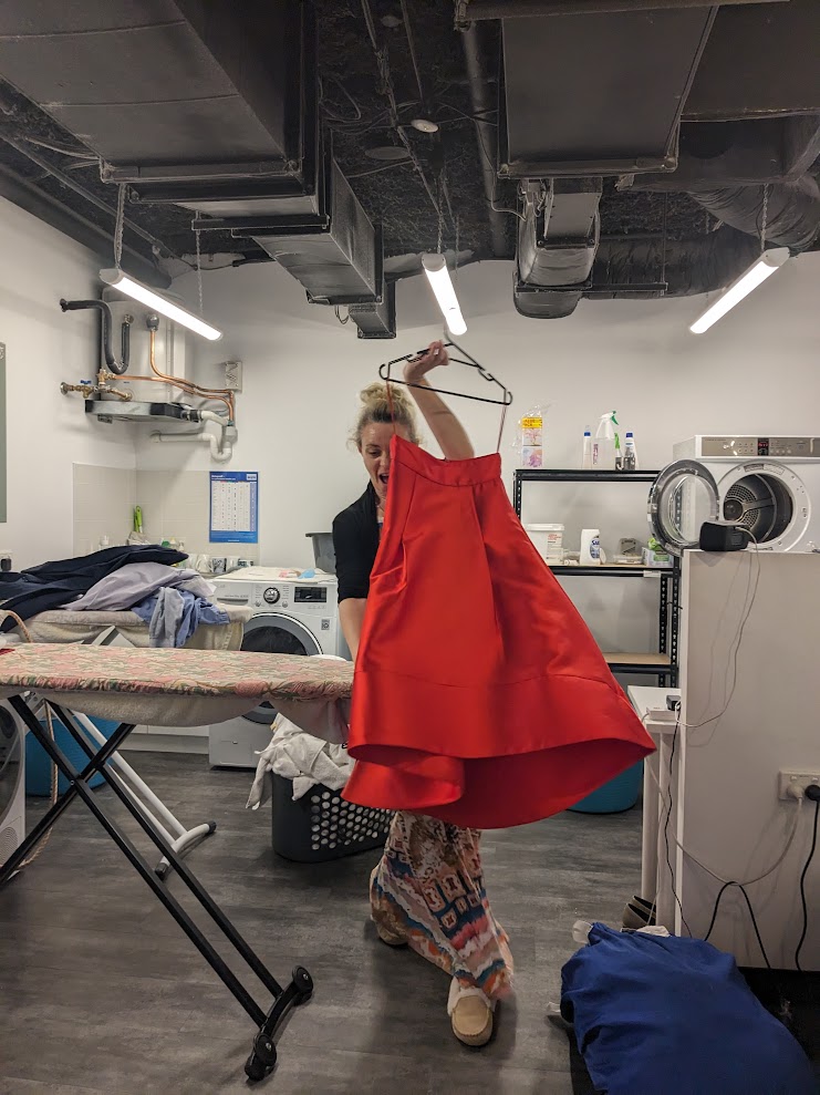 A finished red custom dress held up on a hanger after pressing