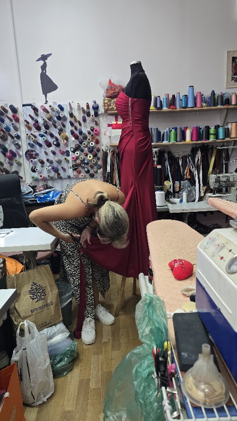 A maker fitting a red gown on a mannequin in her atelier