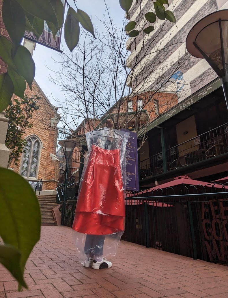 A red custom garment in a protective bag being hand-delivered through the city